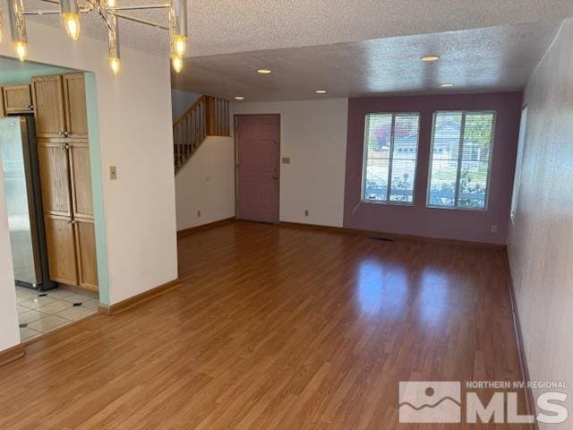 6700 Sandia Dr, Reno, NV 89523 - unfurnished living room with a textured ceiling, stairs, light wood-style flooring, a chandelier, and baseboards