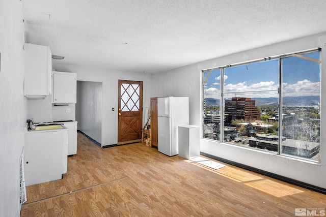 280 Island Ave Unit 1802, Reno, NV 89501 - kitchen featuring a textured ceiling, light wood-style flooring, freestanding refrigerator, white cabinetry, and a view of city