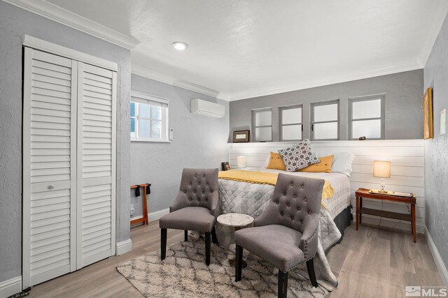 bedroom featuring a wall mounted air conditioner, ornamental molding, baseboards, wood finished floors, and a closet