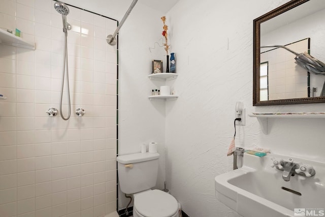 bathroom featuring a sink, toilet, and a tile shower