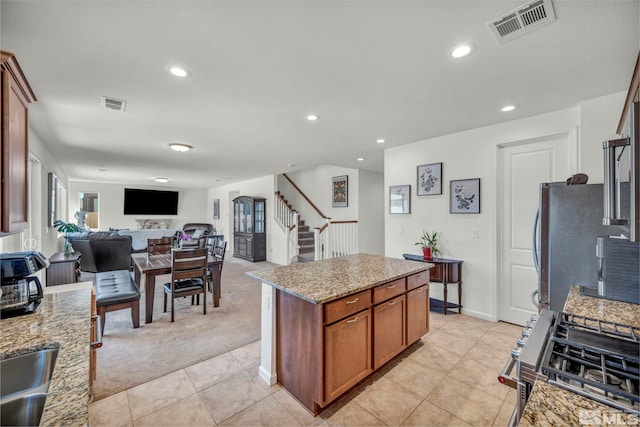 7836 Tarkio Ct, Sparks, NV 89436 - kitchen featuring stainless steel gas range oven, light colored carpet, brown cabinetry, a kitchen island, and light stone counters