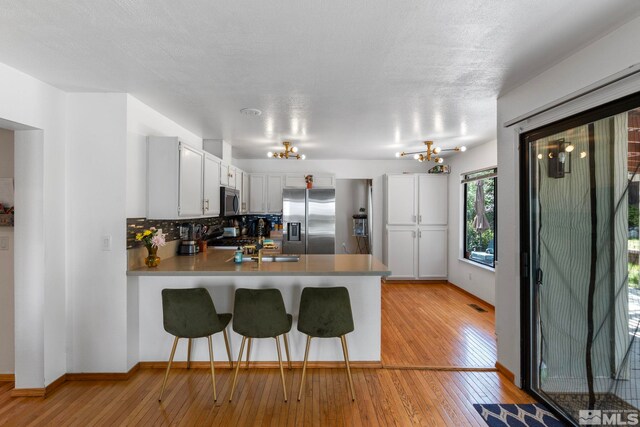 5276 Simons Dr, Reno, NV 89523 - kitchen with stainless steel appliances, a peninsula, a chandelier, light wood finished floors, and a textured ceiling