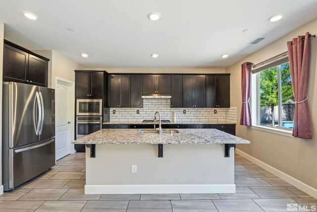 1680 Verdi Vista Ct, Reno, NV 89523 - kitchen featuring stainless steel appliances, backsplash, a kitchen bar, light stone countertops, and a center island with sink