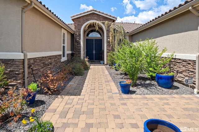 doorway to property featuring stucco siding, stone siding, and a tiled roof