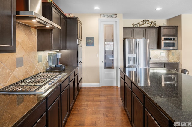 kitchen featuring wall chimney exhaust hood, appliances with stainless steel finishes, baseboards, dark brown cabinetry, and dark wood-type flooring
