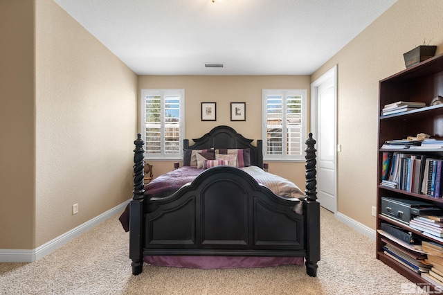 bedroom featuring multiple windows, light colored carpet, baseboards, and a textured wall