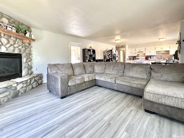 living area with light wood-style flooring and a stone fireplace