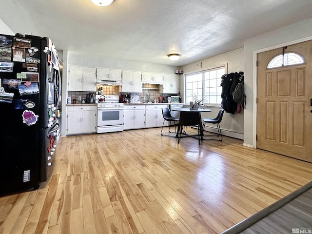 kitchen with white gas range oven, freestanding refrigerator, white cabinetry, under cabinet range hood, and light wood-type flooring