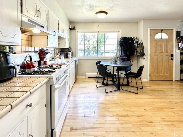 kitchen featuring white range with gas stovetop, under cabinet range hood, tile countertops, light wood-type flooring, and baseboards