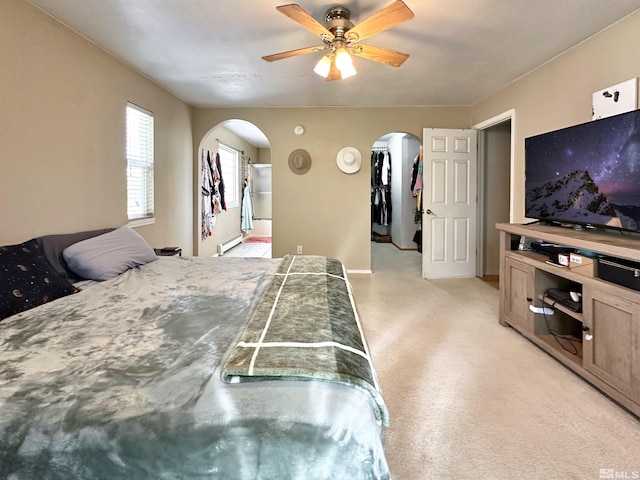 bedroom featuring arched walkways, a baseboard radiator, a spacious closet, and light colored carpet