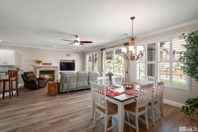 dining area with light wood-type flooring, plenty of natural light, baseboards, a glass covered fireplace, and crown molding