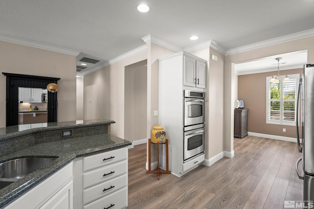 kitchen with stainless steel appliances, light wood finished floors, baseboards, white cabinets, and ornamental molding