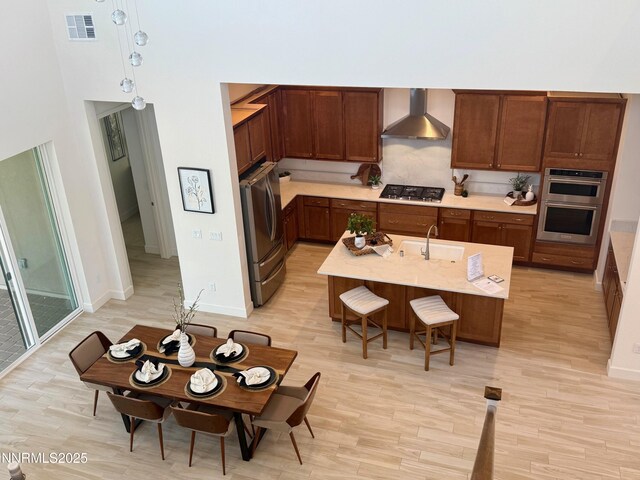 606 Braided Rope Dr, Reno, NV 89511 - kitchen with wall chimney range hood, stainless steel appliances, light wood finished floors, light countertops, and a kitchen island with sink
