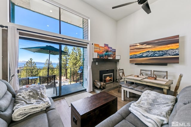 living room featuring wood finished floors, a lit fireplace, a ceiling fan, and a high ceiling