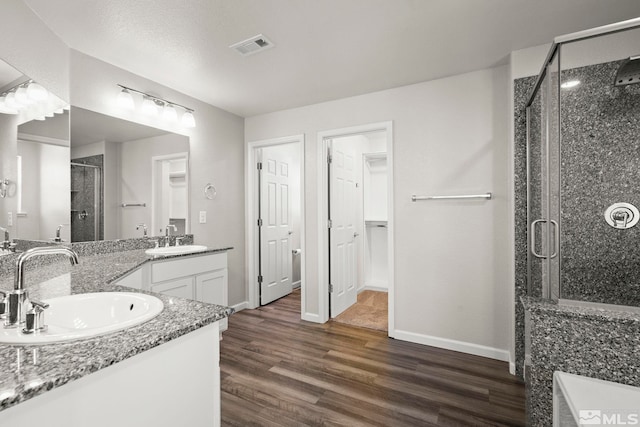 full bath featuring a shower stall, wood finished floors, double vanity, and baseboards