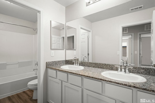 bathroom featuring toilet, wood finished floors, shower / bathtub combination, and double vanity