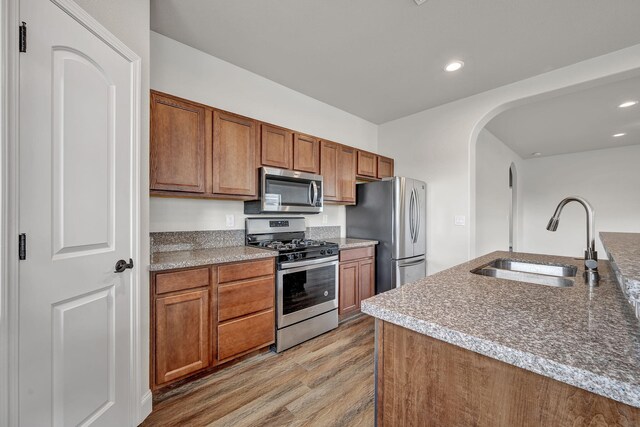 1282 Onda Verde Dr, Fallon, NV 89406 - kitchen featuring appliances with stainless steel finishes, a sink, light wood-style flooring, brown cabinets, and arched walkways