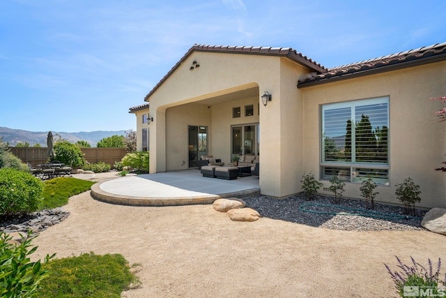rear view of property with a patio, an outdoor living space, fence, stucco siding, and a mountain view
