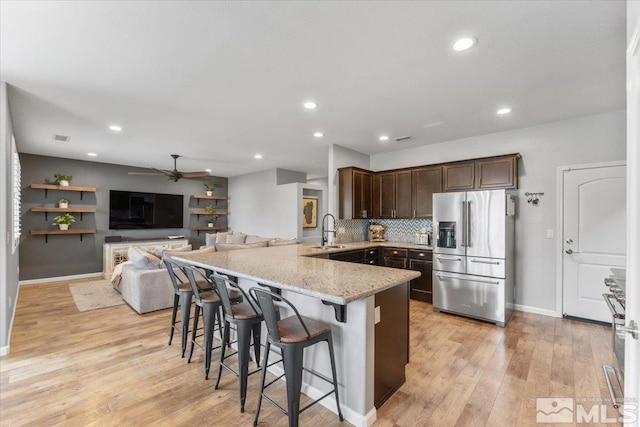 kitchen with premium appliances, a sink, a peninsula, dark brown cabinets, and light stone counters