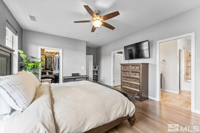bedroom with wood finished floors, a walk in closet, baseboards, a closet, and a ceiling fan