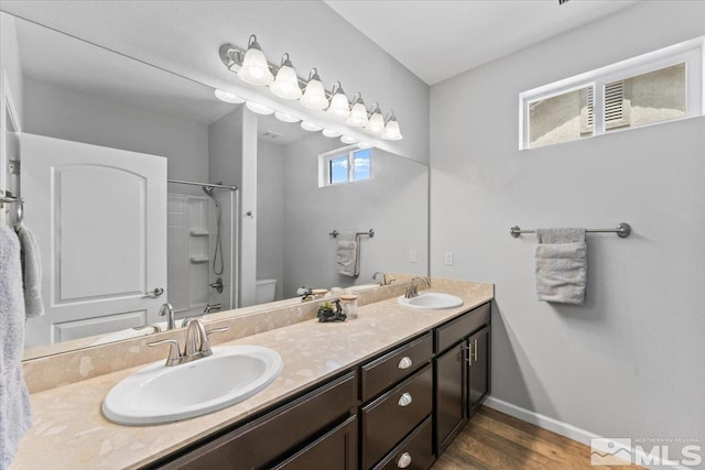 full bath featuring toilet, double vanity, wood finished floors, and baseboards