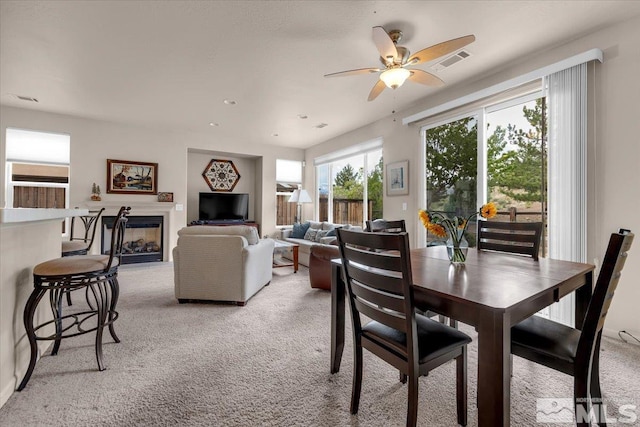 dining space with light carpet, ceiling fan, and a glass covered fireplace