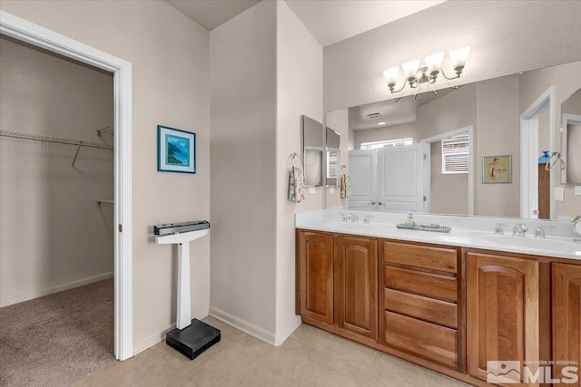 bathroom with a spacious closet, double vanity, a chandelier, and baseboards