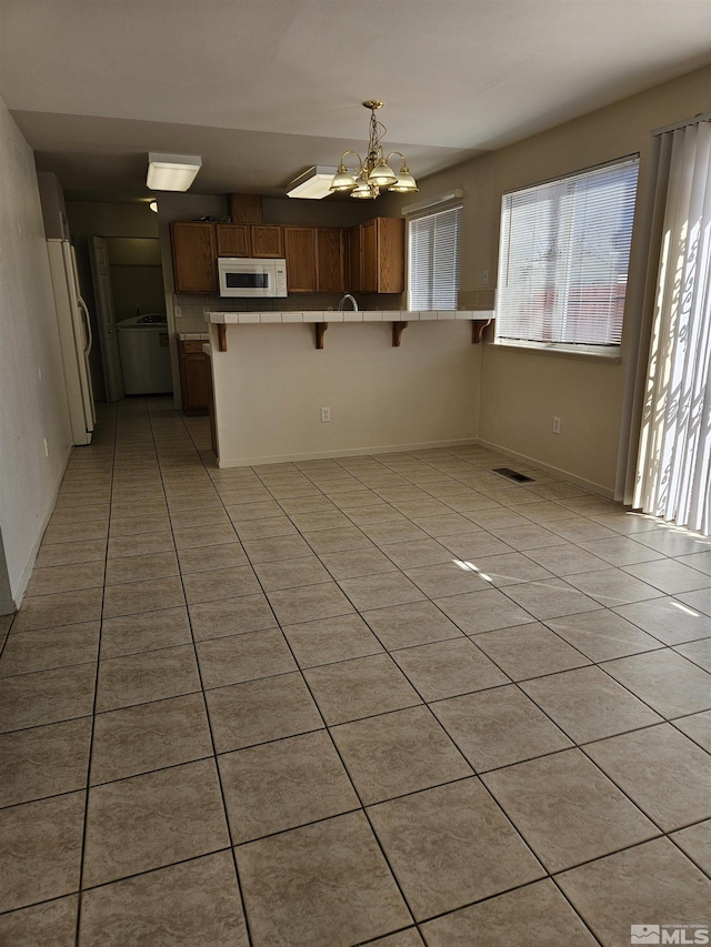 9995 Brightridge, Reno, NV 89506 - kitchen featuring white appliances, a kitchen bar, light tile patterned floors, a peninsula, and brown cabinets