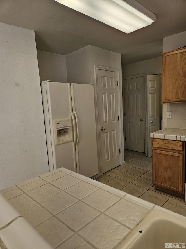 9995 Brightridge, Reno, NV 89506 - kitchen with white refrigerator with ice dispenser, tile countertops, light tile patterned floors, brown cabinetry, and tasteful backsplash