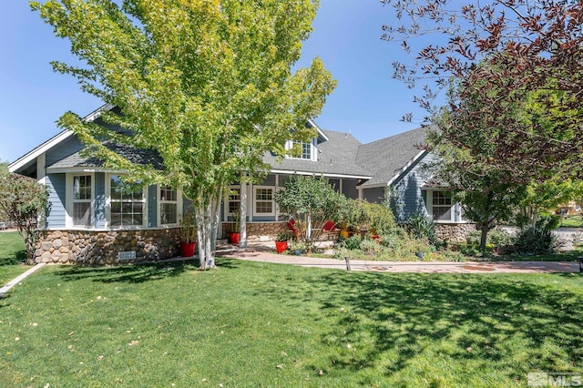 view of property hidden behind natural elements featuring stone siding, a front lawn, and a shingled roof