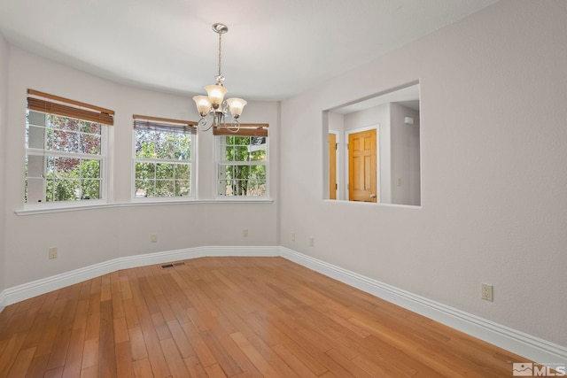 spare room with a chandelier, baseboards, and light wood-style floors