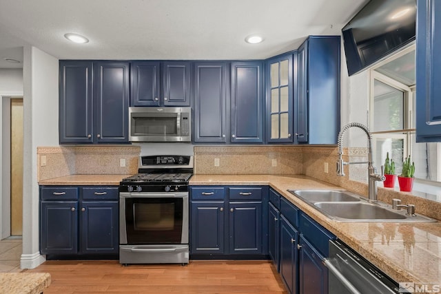 kitchen with appliances with stainless steel finishes, blue cabinetry, a sink, light countertops, and light wood finished floors