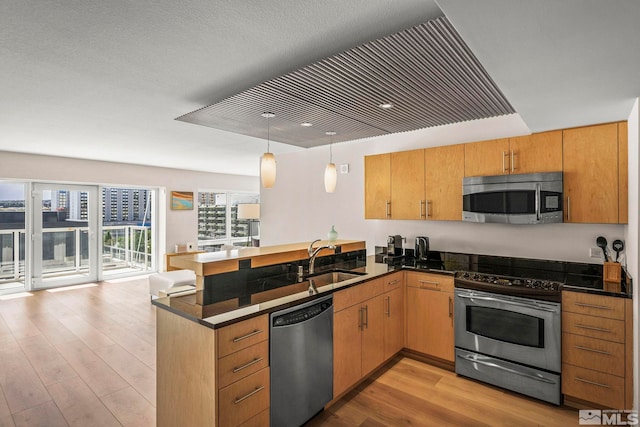 kitchen with appliances with stainless steel finishes, a sink, a peninsula, light wood-style floors, and dark countertops