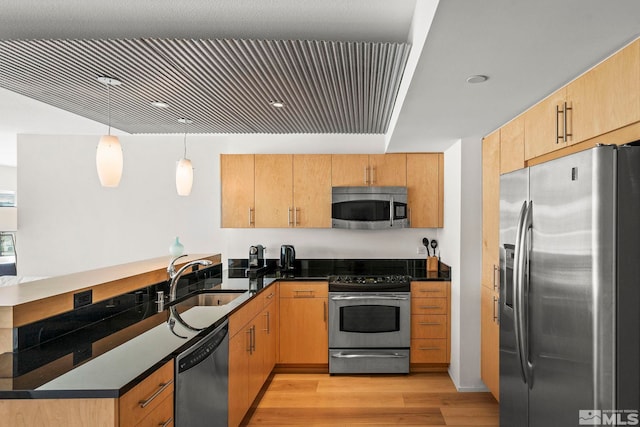 kitchen with stainless steel appliances, a peninsula, light wood-style floors, a sink, and dark countertops