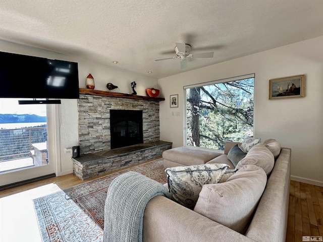living room featuring light wood-type flooring, a ceiling fan, a fireplace, baseboards, and a textured ceiling