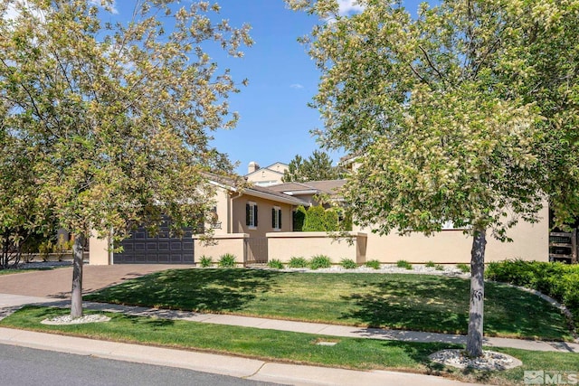 view of property hidden behind natural elements with stucco siding, driveway, an attached garage, and a front lawn