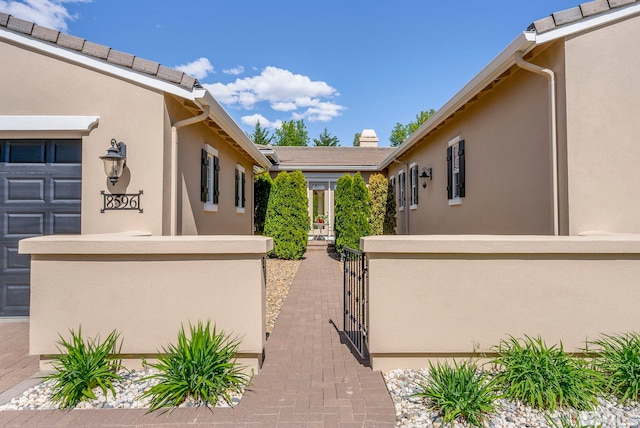 entrance to property with stucco siding, a gate, and fence