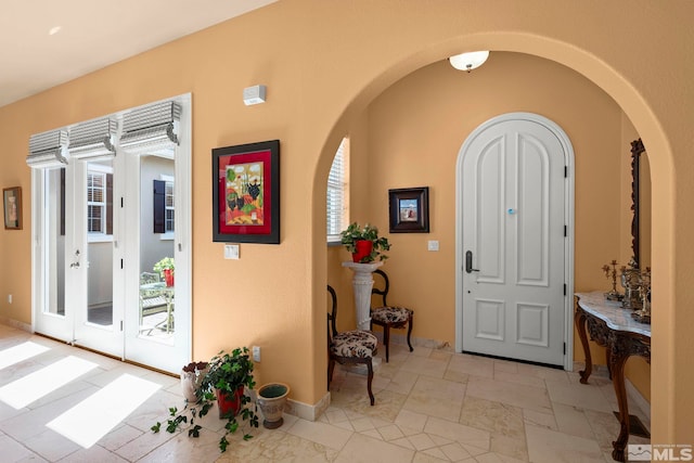 foyer with stone tile flooring, arched walkways, and baseboards