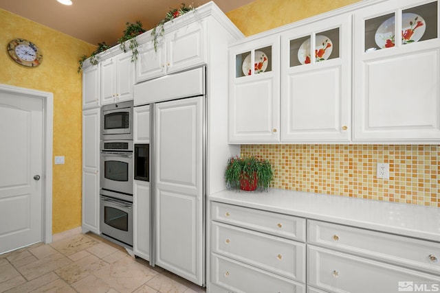 kitchen featuring built in appliances, light countertops, white cabinetry, and decorative backsplash