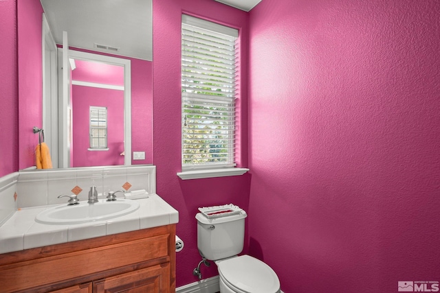 half bathroom with toilet, a textured wall, and vanity