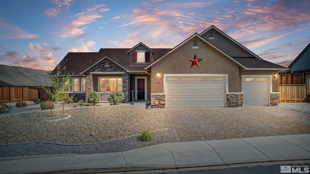view of front of property with stone siding, stucco siding, decorative driveway, an attached garage, and fence