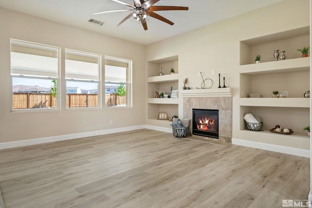 unfurnished living room with built in shelves, ceiling fan, baseboards, a tiled fireplace, and wood finished floors