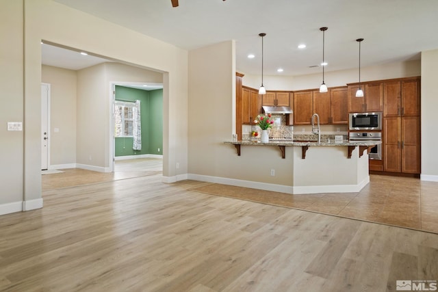 kitchen with appliances with stainless steel finishes, a kitchen bar, brown cabinets, a peninsula, and under cabinet range hood