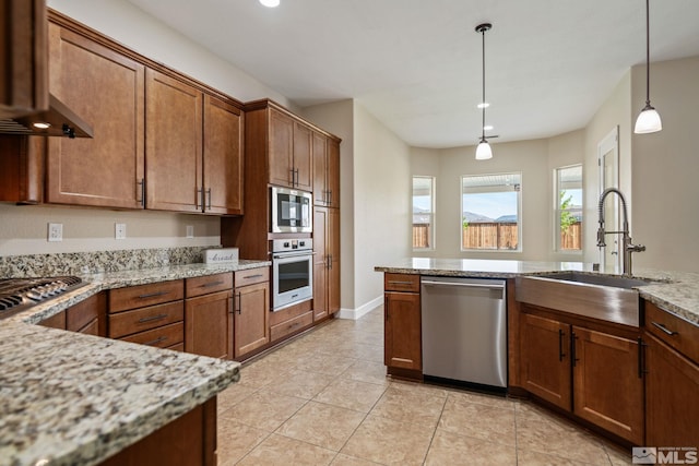 kitchen featuring stainless steel appliances, a sink, decorative light fixtures, light stone countertops, and brown cabinetry