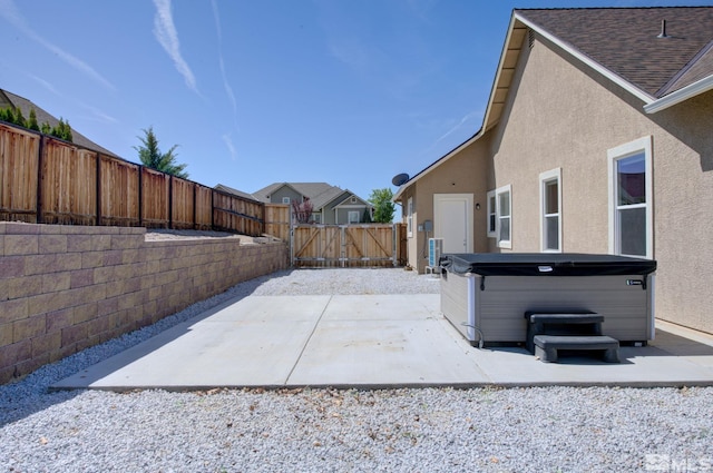 view of patio / terrace featuring a hot tub, a fenced backyard, and a gate