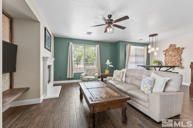 living area featuring a ceiling fan, dark wood-style floors, a glass covered fireplace, and baseboards