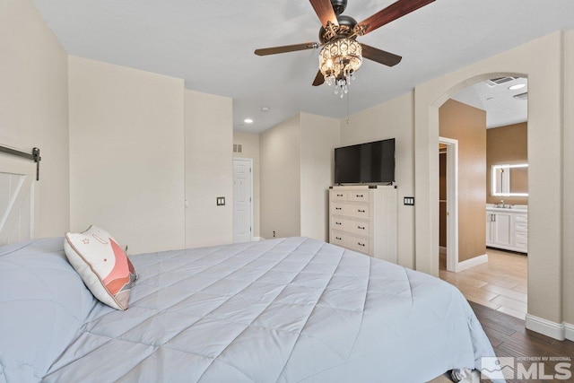 bedroom featuring wood finished floors, arched walkways, baseboards, a sink, and a ceiling fan
