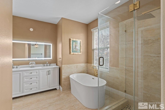 bathroom with a shower stall, tile walls, a freestanding tub, double vanity, and wainscoting