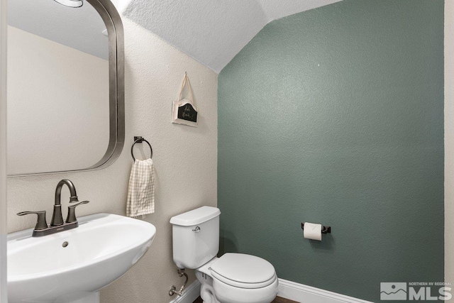 half bath with a sink, lofted ceiling, toilet, and baseboards