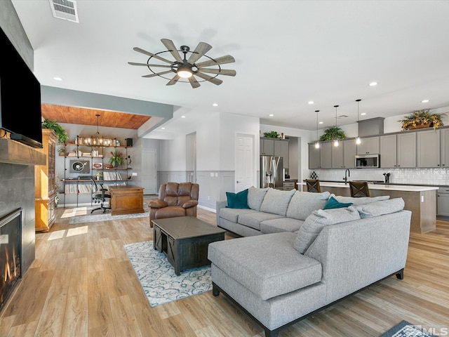 living area with a tiled fireplace, light wood-style flooring, wainscoting, ceiling fan, and a chandelier